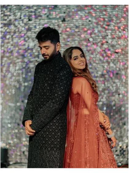 A fun and stylish back-to-back pose against a glittering sangeet backdrop.