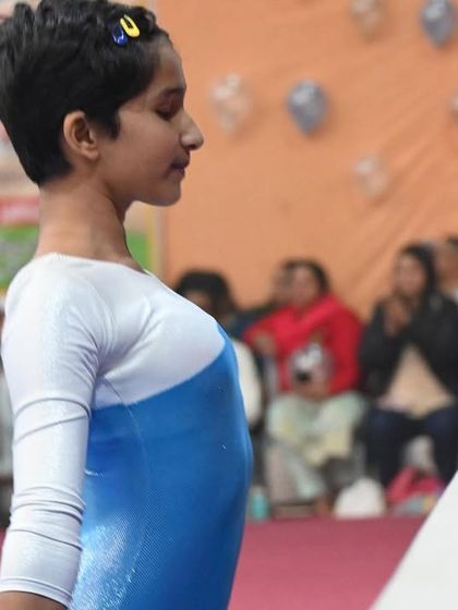 A young gymnast in a moment of quiet focus before her balance beam routine at a competition.