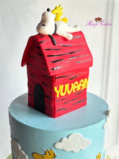 A close-up of the handcrafted, edible Snoopy doghouse topper. Snoopy and his friend Woodstock are relaxing on top of the red house, which is personalized with the birthday boy's name.