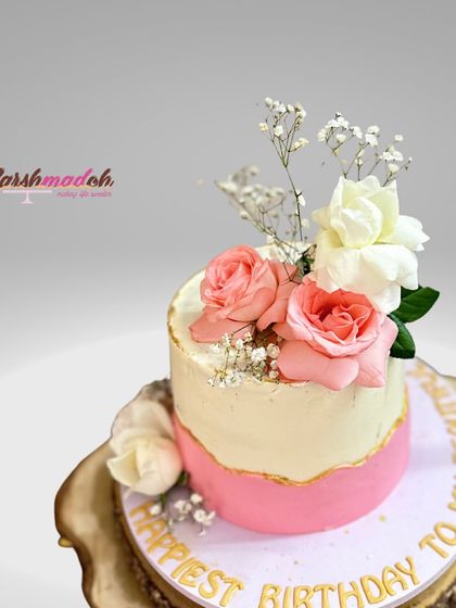 A beautiful birthday cake with a two-tone pink and white design, gold leaf accents, and a lovely arrangement of fresh roses.