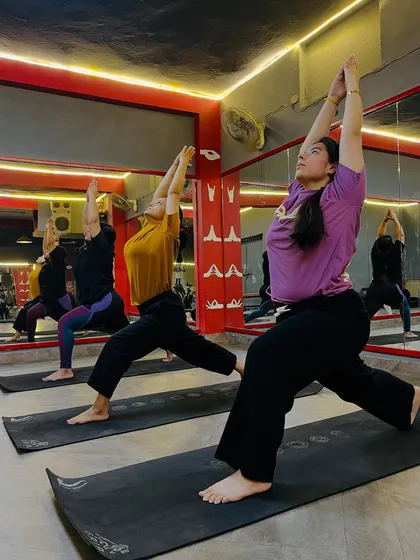 Students holding Virabhadrasana I (Warrior I Pose) in a group class. This pose builds strength in the legs and opens the chest.