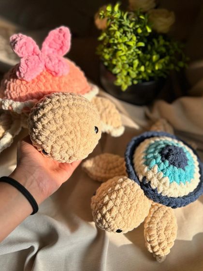 Two of our most popular large turtle designs: one with an evil eye shell for protection and good vibes, and another with a pink butterfly bow for a touch of sweetness.