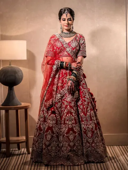 A full-length shot of the bride, showcasing her intricate red lehenga. The makeup is elegant and timeless, a perfect match for her regal attire.