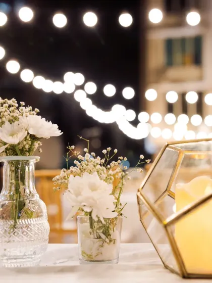It's all about the ambiance. A close-up of the table decor, showing delicate baby's breath in vintage-style vases and geometric candle holders against a backdrop of twinkling lights.