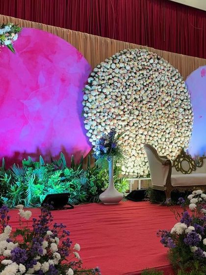 A modern and colorful stage with three large circular backdrops. The mix of a floral wall, a lit-up pink panel, and a blue panel creates a vibrant and artistic setting for a reception.