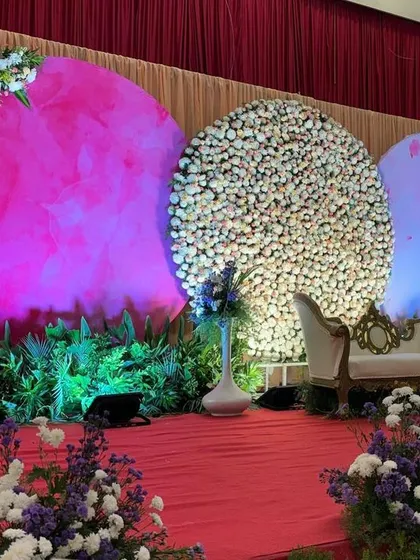 A modern stage with three large circular backdrops, one with a magenta screen and two made of dense white flowers.