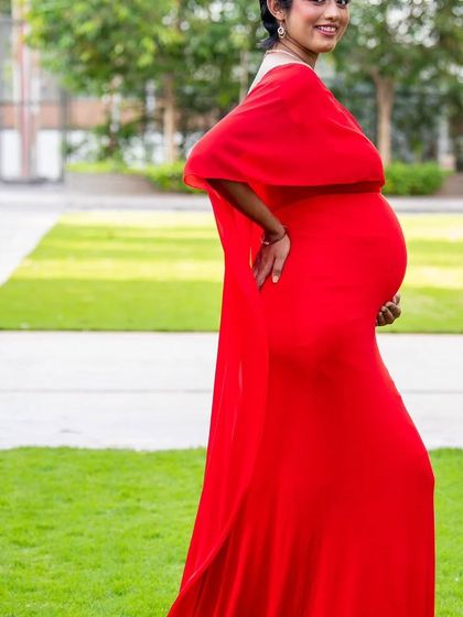 A side view of the red A-line gown with an attached cape. This style is sleek, comfortable, and provides a beautiful pop of color for outdoor maternity photos.