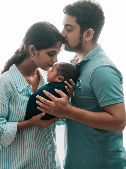 The whole family together, sharing a quiet moment of love. The father kisses his wife's forehead as they both hold their precious newborn, creating a portrait full of warmth.