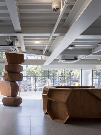 The lobby of the Museum of Art and Photography (MAP), featuring a faceted wooden reception desk and a large totemic sculpture. This entrance space immediately introduces the themes of art, craft, and material that are explored throughout the building.