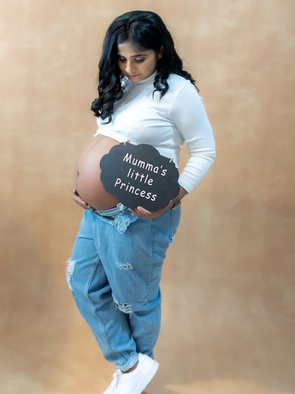 A casual and modern studio portrait of a mom-to-be cradling her bare bump, with a "Mumma's little Princess" sign.