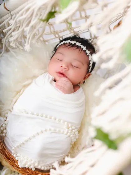 A close-up shot of the baby in the white teepee setup, showing the delicate pearl details on the swaddle and the baby's peaceful expression.