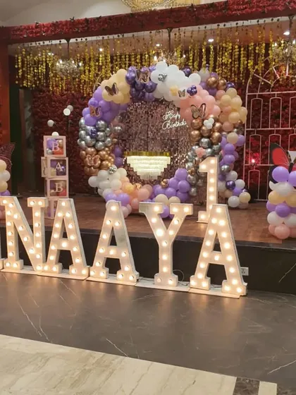 A spectacular butterfly-themed first birthday with large marquee letters spelling "INAAYA" and a balloon ring against a shimmering backdrop.