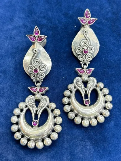 Pure silver chandelier earrings with a traditional design. This pair features intricate silver work with peacock motifs and pink stone accents, creating a beautiful dangling effect.