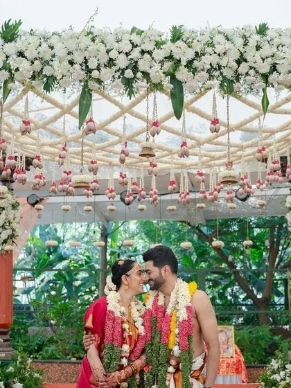We believe in creating picture-perfect moments. Here, the couple shares a quiet moment under a custom-designed mandap, rich with fresh white orchids and traditional hanging bells, embodying the blend of intimacy and grandeur we strive for in our South Indian wedding designs.