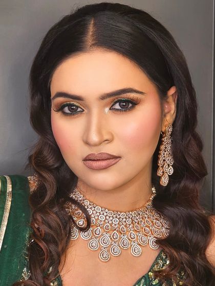 A soft and subtle glam look in a green ensemble. The makeup features a golden shimmer on the eyes, rosy cheeks, and a nude-brown lipstick for an understated yet elegant appearance.