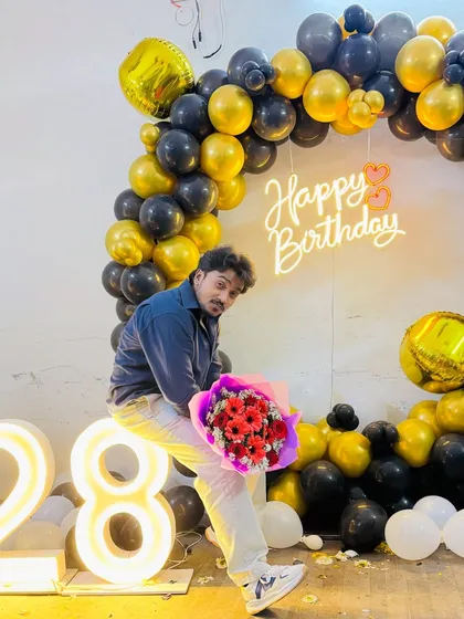 The birthday person posing with flowers in front of their 28th birthday balloon backdrop.