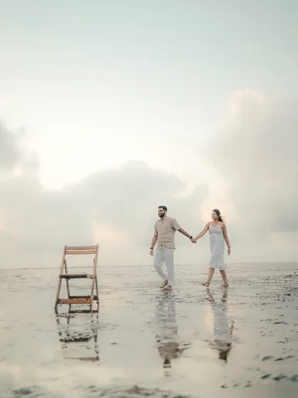 An artistic and minimalist shot of a couple walking on the beach. The empty chair adds a touch of surrealism and intrigue to this unique pre-wedding photo.