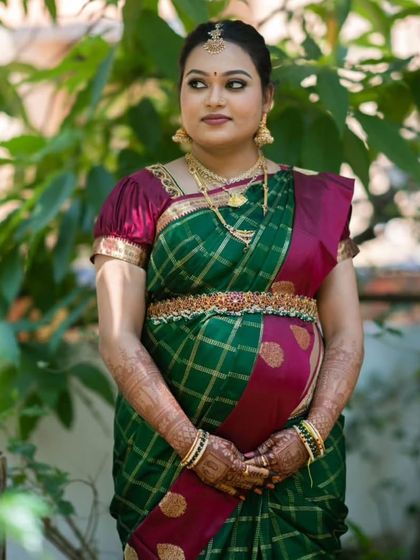 The beautiful Kruthika at her baby shower. Her makeup is soft and traditional, enhancing her natural glow and complementing her green and maroon silk saree.