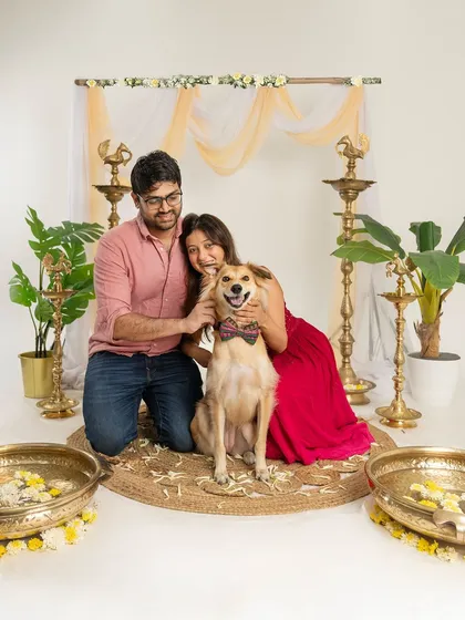 A happy couple cuddles with their smiling dog in a beautifully decorated studio for a Diwali photoshoot. A wonderful way to include pets in the festive celebrations.
