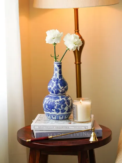 A cozy corner featuring a blue and white vase on a stack of books next to a lit candle. The warm lamplight creates an intimate and peaceful ambiance, perfect for showcasing decor items.
