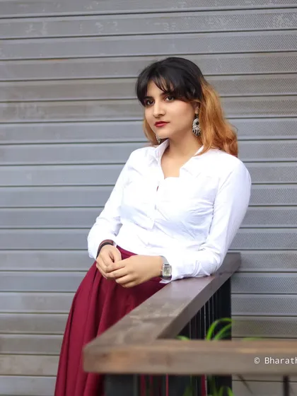 A portrait of the model leaning against a railing, looking directly at the camera. The industrial-style background contrasts with the classic outfit.