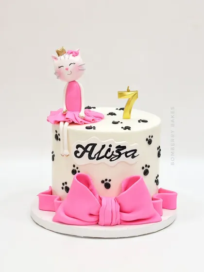 A sweet and simple cat-themed cake for a 7th birthday, featuring a cute kitty ballerina figurine and paw prints.