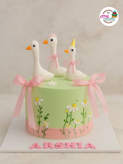 This charming cake features three little geese in a field of hand-painted daisies. The delicate pink ribbons and soft green frosting create a sweet and whimsical look for a special birthday.