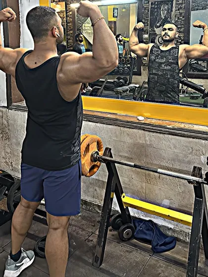 Checking bicep and shoulder definition in the gym mirror. I coach clients on how to properly flex and pose to track their own progress.