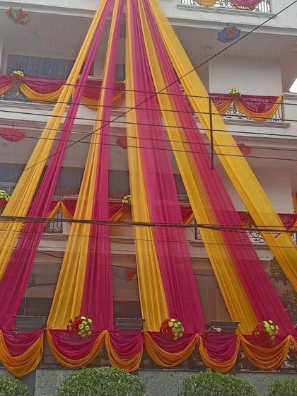 A full view of a house decorated with bright yellow and pink drapes, creating a very traditional and festive 'shaadi wala ghar' feel.