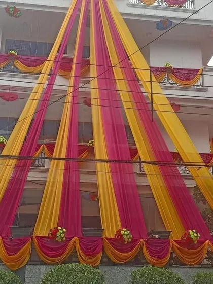 A full view of a house decorated with bright yellow and pink drapes, creating a very traditional and festive 'shaadi wala ghar' feel.
