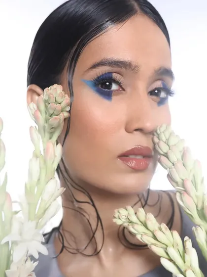 This shot showcases the sharp, angular shape of the blue graphic liner, complemented by glossy lips and glowing skin.