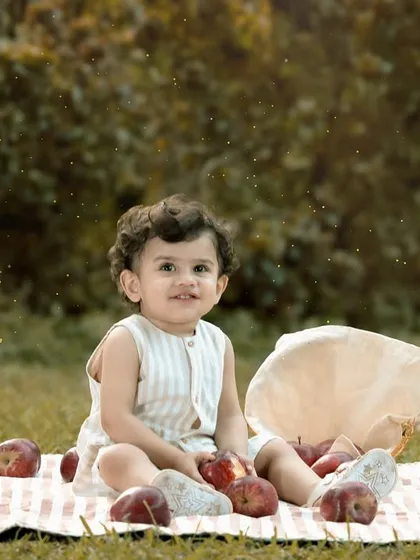 A one-year-old boy sits on a picnic blanket in a park, surrounded by apples. This outdoor milestone shoot uses natural elements to create a fresh and timeless birthday portrait.