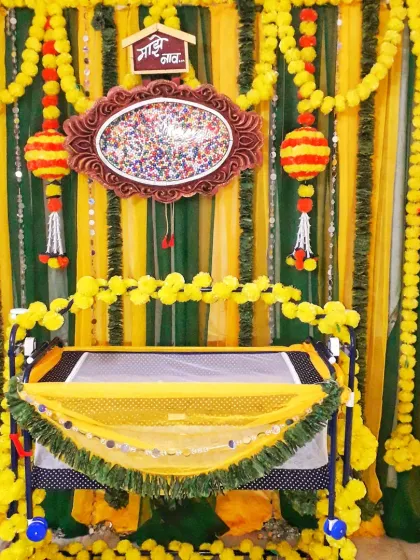 This is a traditional naming ceremony (barsa) decoration. The baby's cradle (palna) is decorated with yellow flowers, and the backdrop uses marigold garlands and green drapes for a classic look.