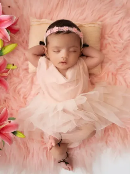 A beautiful overhead shot of a newborn girl in a pink dress, lying on a soft rug and framed by pink lilies and peonies. This setup creates a dreamy, fairytale-like portrait.