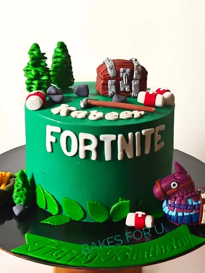 A Fortnite-themed cake for a new teenager, featuring edible elements from the popular game like the treasure chest, piñata, and trees. The vibrant green base captures the look of the game's landscape.