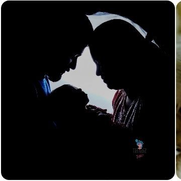 A dramatic and artistic silhouette of a new family, their heads bowed together over their baby. This creates a powerful feeling of love and intimacy.