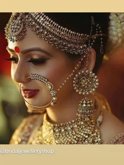 A side profile of a bride showing off her elaborate matha patti, oversized earrings, and nath. This highlights the beautiful details of a complete bridal jewellery set.