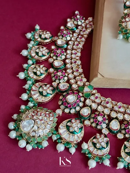Look closely at the artistry in this Kundan necklace. Each stone is carefully set by our karigars, blending emerald green, ruby red, and lustrous pearls. This is the fine detailing and craftsmanship that we stand for in every piece.
