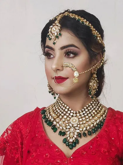 A classic bridal look with a Kundan and emerald necklace against a red blouse. The simple red bindi completes this timeless aesthetic.