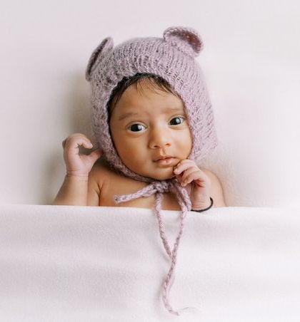 A sweet baby girl in a knitted bear bonnet, awake and looking right at the camera. Her curious expression is a beautiful memory from her newborn session.