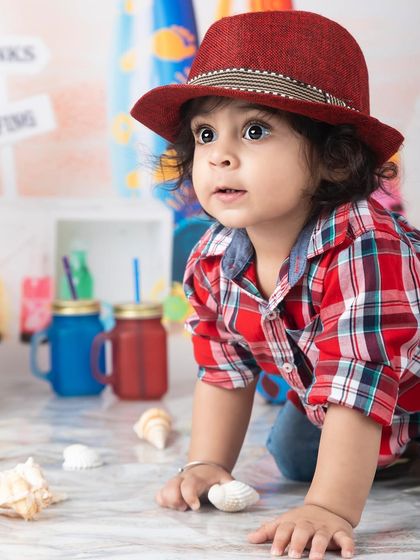 This little boy in his red plaid shirt and fedora is exploring the shells at our beach setup.