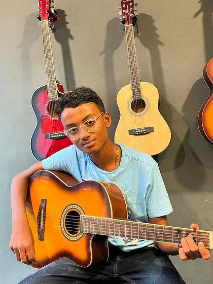 A young guitarist proudly poses with his instrument during a lesson. We aim to make learning fun and build confidence in our students from day one.