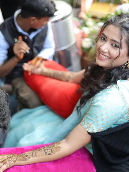 The bride smiles happily while getting her intricate Mehndi design applied.