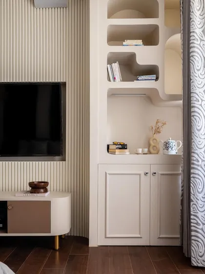 This bedroom blends warmth and elegance. Off-white wainscoting adds timeless charm, while teak flooring grounds the space in comfort. The custom-built shelving with its unique organic shapes adds personality.