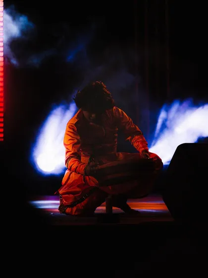 A lone performer crouches on stage, surrounded by dramatic backlighting and smoke. I use these elements to create a moody, cinematic atmosphere in my performance photography.