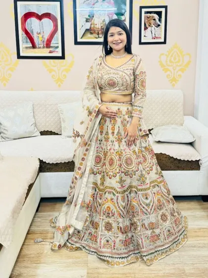 An elegant off-white lehenga with colorful traditional motifs. This rental is a sophisticated and artistic choice for a wedding guest.