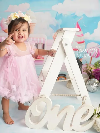 A proud one-year-old stands next to a large letter 'A', pointing with a cheeky smile. These props add a fun, interactive element to milestone sessions.