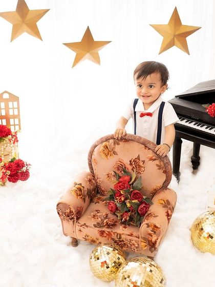 A happy boy standing by his floral armchair. The bright, clean background and festive props make this a joyful and celebratory portrait.