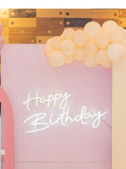 A soft and modern birthday backdrop in pastel pink. The custom neon "Happy Birthday" sign and organic balloon garland create a stylish and celebratory photo spot.