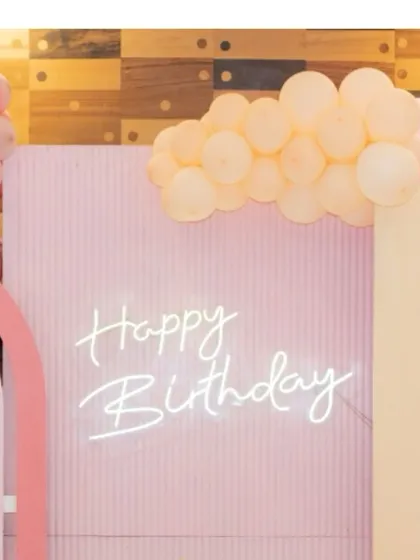 A soft and modern birthday backdrop in pastel pink. The custom neon "Happy Birthday" sign and organic balloon garland create a stylish and celebratory photo spot.